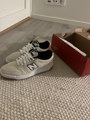 Vita New Balance 550 sneakers - Snygga vita New Balance 550 sneakers med svart detalj och klassisk N-logga på sidan. Ovandelen är i mocka och mesh för en fräsch look, och yttersulan är i gummi med coolt mönster. Perfekta för dig som gillar streetwear och sportig stil.