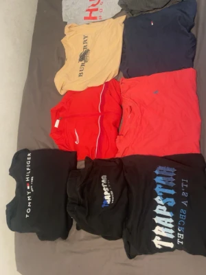 T-shirtpaket med märken: Trapstar, Burberry, Hugo Boss - Säljer ett paket med flera t-shirts från Trapstar, Burberry, Hugo Boss, Tommy Hilfiger och Nike. Färgerna är svart, grå, beige, marinblå och röd. T-shirtsen har tryck och loggor, vissa är kortärmade och i bomull. Perfekt för dig som gillar streetwear och märkeskläder.