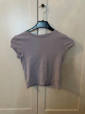 Ljuslila croppad t-shirt - En enkel och stilren ljuslila croppad t-shirt med rund halsringning och korta ärmar. Tillverkad i mjuk bomull som känns skön mot huden. Köpt från HM och är i fint skick