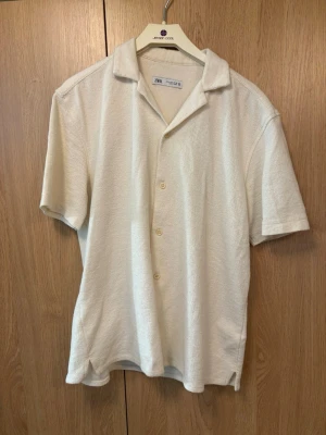 Vit kortärmad skjorta från Zara - Stilren vit skjorta från Zara med korta ärmar och klassisk krage. Skjortan har knappar framtill och är tillverkad i bomullsmaterial. Perfekt för en avslappnad och fräsch look.