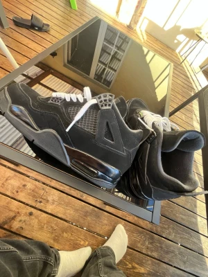 Svarta Air Jordan 4 Retro sneakers - Säljer ett par svarta Air Jordan 4 Retro sneakers med vita skosnören och meshdetaljer på sidorna. Skorna har en hög siluett, synlig Air-enhet i sulan och detaljer i mocka och plast. Perfekta för dig som gillar klassisk streetwearstil.