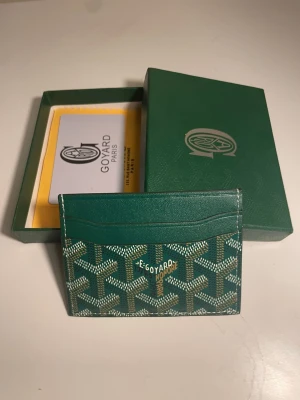 Grön kortfodral från Go4yard - Snyggt grönt kortfodral från Go4yard med det klassiska mönstret i vitt och beige. Tillverkad i tåligt läder och har flera fack för kort. Kommer med original ask och certifikat. Perfekt för dig som vill ha något exklusivt och stilrent i fickan.