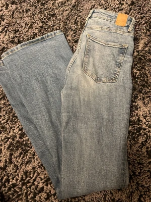 Ljusblå raka jeans från Bershka - Säljer ett par ljusblå jeans från Bershka med klassisk femficksmodell och raka ben. Jeansen har en tvättad look och är tillverkade i denim med tydliga sömmar och läderpatch bak i midjan. Perfekta för en avslappnad och trendig stil.