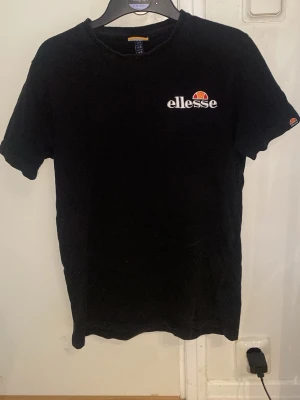 Svart Ellesse t-shirt med logga - Snygg svart t-shirt från Ellesse med klassisk logga tryckt på bröstet och ärmen. T-shirten har rund hals och korta ärmar, perfekt för en avslappnad och sportig stil. Tillverkad i mjuk bomull för skön komfort.