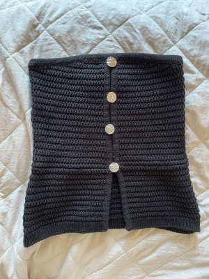 Svart tubtopp med knappar - Snygg svart tubtopp med fyra dekorativa silverfärgade knappar framtill. Toppen är ribbad/stickad, använd enska gång 