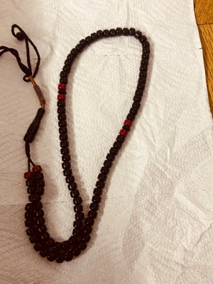 Svart misabaha med röda pärlor - Snyggt misabaha med svarta pärlor och några röda detaljer. Misabaha har en enkel design med rundade pärlor trädda på en svart tråd och knytning i änden. Perfekt för dig som gillar stilrena accessoarer med en liten färgklick.