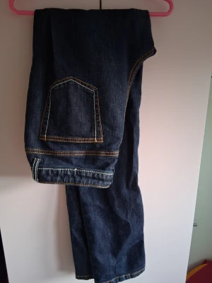 Mörkblå jeans med fickdetalj - Säljer ett par mörkblå jeans med cool fickdetalj på benet och kontrastsömmar. Jeansen har raka ben och är gjorda i klassiskt denimtyg. Perfekta för dig som gillar en avslappnad och stilren look.