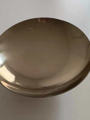 Guldfärgad metallskål från H&M Home - Snygg guldfärgad skål i metall från H&M Home. Skålen har en rund form och en blank finish som ger ett stilrent intryck. Perfekt som dekoration eller förvaring av småsaker. Märkningen syns undertill.