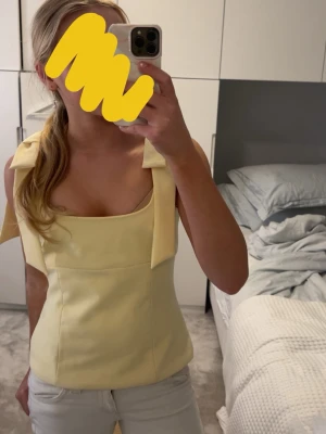 Gul linnetopp med rosettband - Snygg ljusgul linnetopp med breda axelband som knyts i rosetter. Toppen har en rak, figurnära passform och fyrkantig urringning. Perfekt för varma dagar och enkel att styla med jeans eller kjol. 💛💞🥂