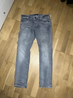 Jack & Jones  - Säljer ett par gråa jeans i Slim fit. Jeansen har en snygg tvättad look och är perfekta för en avslappnad stil. Materialet är denim med lite stretch för extra komfort. Storlek 31 32
