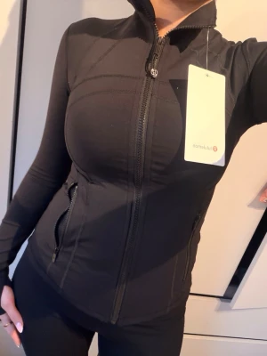 Svart träningsjacka från Lululemon - Slimmad svart träningsjacka från Lululemon med hög krage. Priset är prutat och klart