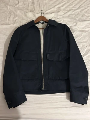 Mörkblå jacka med dragkedja - Stilren mörkblå jacka med klassisk krage och stora fickor framtill. Jackan har dragkedja och knappar vid ärmslut och midja. PRIS KAN DISKUTERAS!