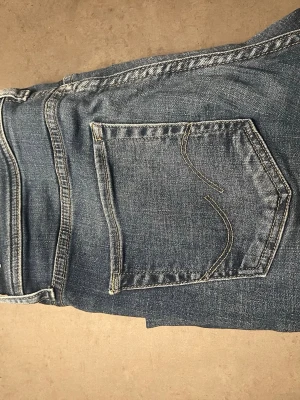 Blå raka jeans från Jack and Jones  - Säljer ett par klassiska blå jeans från     Jack and Jones med raka ben och femficksmodell. Jeansen har snygga slitningar.Tillverkade i mjuk och slitstark denim, perfekta till vardagslooken.