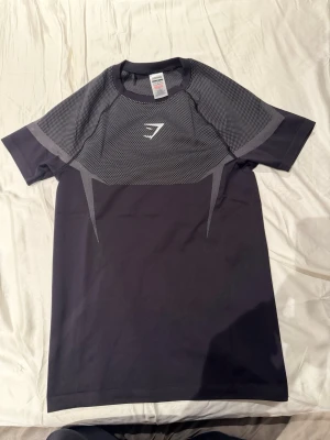 Svart onyx v5 T-shirt från Gymshark - Svart och grå onyx v5 T-shirt från Gymshark med korta ärmar och sportig design. Tillverkad i polyester och elastan för bra stretch och andningsförmåga. Snyggt mönstrad upptill och med Gymshark-logga på bröstet. Perfekt för gym och träning. Passar riktigt snyggt och bekväm 