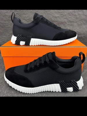 H märkes skor - Stilrena svarta H sneakers med vit, räfflad sula och svarta H-detaljer på sidan och undersidan. Ovandelen är i mesh och mocka för en modern look. Skorna har svarta skosnören och en låg silhuett som passar till streetwear.