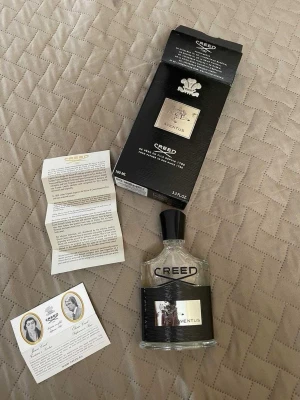 Creed Aventus Eau de Parfum 100ml - Creed Aventus Eau de Parfum är en exklusiv herrdoft i en elegant, genomskinlig glasflaska med svart etikett och silverdetaljer. Flaskan rymmer 100 ml och kommer med originalkartong och informationsblad. Doften är känd för sin lyxiga och fräscha karaktär.