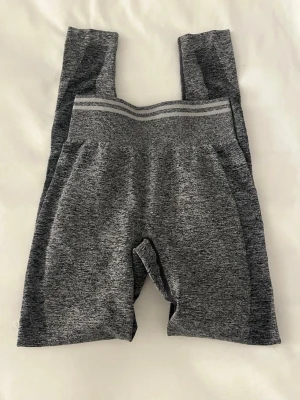 Melerade grå sömlösa leggings - Snygga gråmelerade leggings med hög midja och bred resår. Sömlös design för extra komfort och en tight passform som framhäver benen. Materialet är stretchigt och mjukt, perfekt för träning eller chill. Diskreta ränder upptill vid midjan ger en sportig vibe.