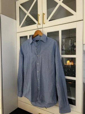 Blå linneskjorta från J.F.K - Snygg blå skjorta från J.F.K. Klassisk krage, knappar framtill och långärmad modell. Perfekt för en avslappnad men stilren look. Skjortan har en rak passform och är enkel att matcha med olika outfits.