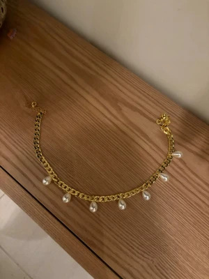 Guldhalsband med pärldroppar - Snyggt halsband i guldfärgad metall med kedja och hängande vita pärldroppar. Perfekt accessoar för att lyfta din outfit med en trendig touch. Halsbandet har en klassisk kedjelänk och sju droppformade pärlor som ger en elegant känsla.