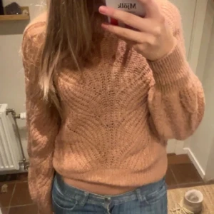 Korallrosa stickad tröja  - Säljer en korallfärgad stickad tröja med snyggt strukturmönster och ribbade muddar. Tröjan har långärmade ballongärmar och en lite croppad passform. Materialet består av en blandning mellan alpacka, ull och polyester! Färgen är också mer rosa i verkligheten, (se sista bild) 🩷