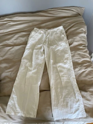 Vita  linnebyxor  - Säljer ett par vita linnebyxor med breda ben och elastisk midja och fickor ifrån Gina tricot young. Byxorna har en avslappnad passform och är tillverkade i ett lätt och luftigt linnetyg, perfekta för varma dagar. De är i storlek 146/152 men de passar även större då de är stretchiga och breda. De har en fläck där bak (se bilden) därav priset men borde gå bort med fläckborttagning eller liknande. 