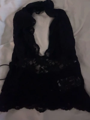 Svart spetslinne  - Snyggt spetslinne med djup urringning. Genomskinligt material med blommigt spetsmönster och dekorativ kant nertill. 