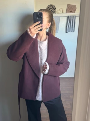 Vinröd kappa med knytskärp - Trendig vinröd kort kappa med bred krage och knytskärp i midjan. Kappan är superfin nu till våren, men tyvärr lite för stor för mig, därför säljer jag den helt oanvänd och med prislapp kvar🌺