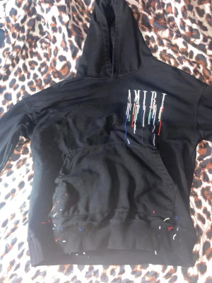 Svart hoodie från Amiri med brodyr - Säljer en svart hoodie från Amiri med färgglada broderade detaljer och logga på bröstet. Hoodien har en stor huva och magficka. Brodyren har inslag av rött, blått, vitt, gult och turkos. Biligare vid snabb affär 