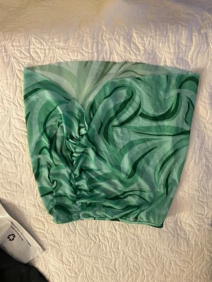 Grön mönstrad kortkjol med rynk - Säljer en snygg grön bad kortkjol med abstrakt mönster i olika gröna nyanser. Kjolen har en rynkad detalj på sidan som ger en cool och trendig look. Perfekt för dig som vill sticka ut lite extra!