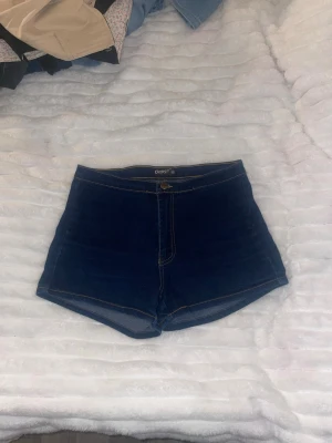 Mörkblå denimshorts från Oopsi - Snygga mörkblå denimshorts från Oopsi med hög midja och klassiska kontrastsömmar. Shortsen har en enkel design utan extra detaljer och är perfekta för varma dagar. Tillverkade i bomull för en bekväm känsla.