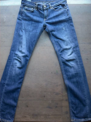 Blå raka Dondup jeans med slitningar - Säljer ett par klassiska blå jeans med raka ben och snygga slitningar på framsidan. Jeansen har fem fickor och kontrastsömmar. Materialet är denim i bomull och de har en tidlös tvättad look som passar till det mesta.