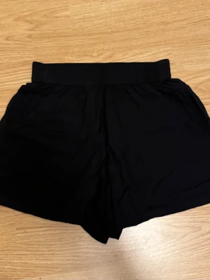 Svarta shorts - Svarta shorts med bred resår i midjan och lös passform. Perfekta för varma dagar och enkla att matcha med olika toppar. Tillverkade i ett lätt och mjukt material som känns skönt mot huden
