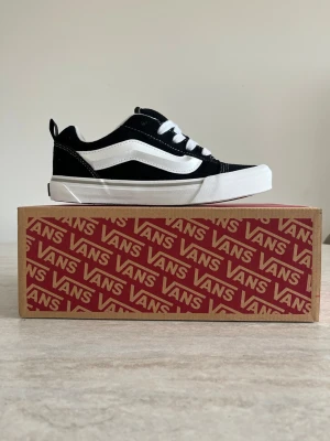 Vans Knu Skool svartvita sneakers - Klassiska Vans  sneakers i svart och vitt med den ikoniska sidoremsan. Ovandel i canvas och mocka, vita snören och vit gummisula. Perfekt för dig som gillar streetwear och skatekultur.