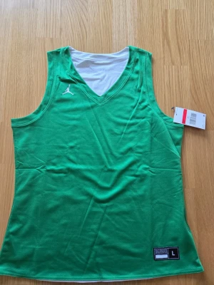 Nike Jordan träningstop , basket , NBA, Dam strorlek L - Snyggt grönt basketlinne från Jordan med vitt innerfoder och klassisk v-ringning. Tillverkat i lätt och ventilerande meshmaterial, perfekt för träning eller match. Ikonisk Jumpman-logga på bröstet och etikett nertill.