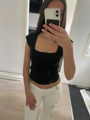 Svart croppad topp med fyrkantig hals - Säljer en svart croppad topp med fyrkantig halsringning och korta ärmar. Toppens passform är tight och den har ett stilrent, minimalistiskt utseende som är lätt att matcha. Perfekt för dig som gillar trendiga och enkla plagg. Använt typ en gång 