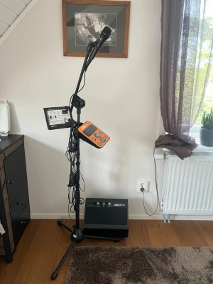 Singtrix karaokesystem med mikrofon - Karaokesystem från Singtrix med mikrofon, stativ och kontrollpanel i orange och svart. Systemet har flera knappar och display för att styra effekter och ljud. Perfekt för att sjunga hemma med vänner. Inkluderar högtalare och sladdar.