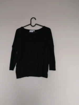 Svart basic tröja med rund hals - En enkel svart långärmad tröja med rund halsringning och avslappnad passform. Perfekt att matcha med jeans eller kjol för en clean look. Tröjan har ribbade muddar vid ärmslut och nederkant.