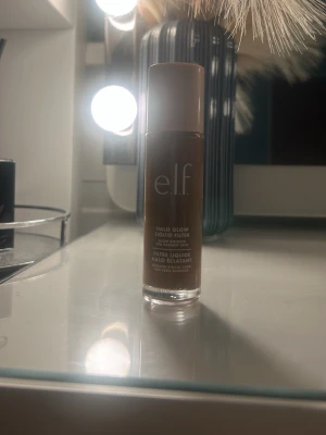 e.l.f. Halo Glow Liquid Filter Rich - e.l.f. Halo Glow Liquid Filter i nyansen Rich (Shade 8). Flytande foundation med glow-effekt i en brun ton. Kommer i en cylinderformad glasflaska med skruvlock. Perfekt för dig som vill ha en naturlig lyster och jämn hudton. Använd 2 gånger som bronzer, så nästan som ny