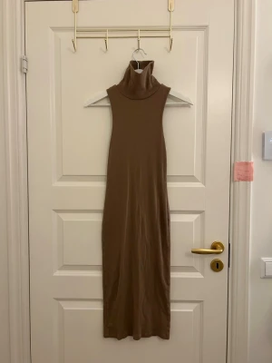 Beige ärmlös långklänning med polokrage - Snygg beige långklänning med polokrage och ärmlös design. Klänningen har en rak passform och är tillverkad i ett mjukt, stretchigt material som sitter bekvämt mot kroppen. Perfekt för dig som gillar stilrena och minimalistiska plagg.