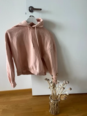 Ljusrosa hoodie med huva XS/S - Ljusrosa hoodie med huva och dragsko. Oversized passform med nedhasade axlar och ribbade muddar. Perfekt för en avslappnad och trendig stil. Mjuk bomullskänsla och enkel att matcha med jeans eller leggings.
