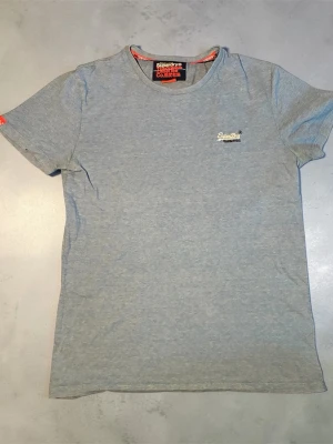 Ljusblå t-shirt från Superdry - Snygg ljusblå  t-shirt från Superdry med liten broderad logga på bröstet. Klassisk passform med rund hals och korta ärmar. Perfekt basic-plagg att ha i garderoben.