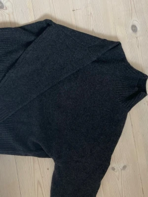 Mörkgrå stickad tröja från Zara - Mysig mörkgrå stickad tröja från Zara med hög hals och ribbade muddar vid ärmslut och nederkant. Perfekt och enkel att matcha med olika outfits. Tillverkad i mjukt material som känns skönt mot huden.