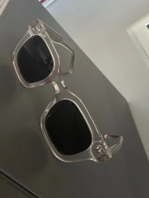 Solglasögon från Allcap1 - Snygga solglasögon med transparent båge och svarta, fyrkantiga linser. Perfekt för dig som vill ha en modern och stilren look. Bågarna är robusta och har en cool, kantig form som sticker ut. Pris är ej hugget i sten så är öppen för prisförslag!