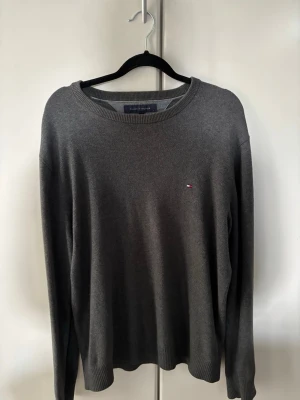 Grå stickad tröja Tommy Hilfiger - Mörkgrå stickad tröja från Tommy Hilfiger, storlek M, skick 8/10, Perfekt för en clean och stilren look.