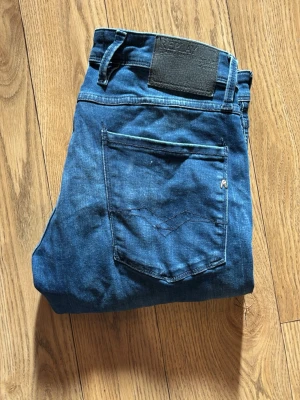 Blå jeans Replay Anbass 32 - Säljer ett par snygga blå jeans från Replay, modell Anbass. Klassisk femficksdesign med tydliga sömmar och Replay-lapp bak i midjan. Jeansen har en modern passform och är tillverkade i slitstarkt denimtyg. Perfekta för dig som gillar stilrena och tidlösa jeans. W32 L32