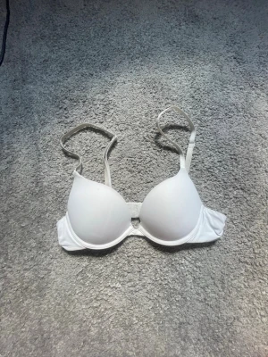 Vit push-up bh  - Säljer en enkel och stilren vit push-up bh med vadderade kupor och justerbara axelband. Bh:n har släta kupor och klassisk form som ger bra stöd och lyft. Perfekt under ljusa toppar och tröjor. Den är från Lindex i storlek 70A i modell MALVA super fint skick och super skön ( står ej för frakt) 