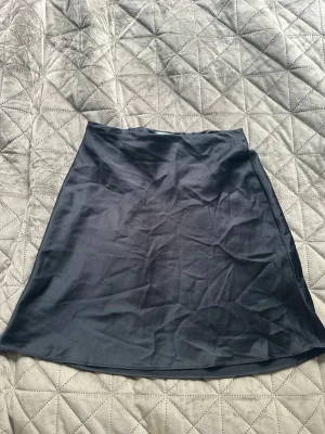 Svart satinkjol från Chiquelle - Snygg svart satinkjol från Chiquelle i storlek S. Kjolen har en lätt A-linjeform och slät yta med diskret glans. Perfekt att styla med en crop top eller stickad tröja för en trendig look.