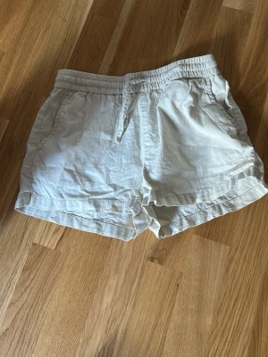 Beiga shorts med dragsko - Snygga beiga shorts med resår och dragsko i midjan. De har två sidofickor och är tillverkade i ett lätt och luftigt tyg, perfekt för varma dagar. Avslappnad passform och uppvikta benslut ger en chill vibe.