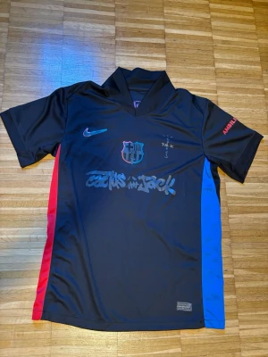 FC Barcelona x Cactus Jack  tröja - Snygg svart FC Barcelona x Cactus Jack tröja  med kort ärm. Har klubbmärke på bröstet, färgdetaljer i rött och blått på sidorna samt Cactus Jack-tryck framtill. Perfekt för dig som gillar unika sportkläder och streetwear. Jag har haft på mig en gång annars de är helt ny