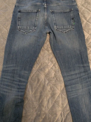 Blå jeans med raka ben - Snygga blå jeans med raka ben och klassisk femficksdesign. Jeansen har en lätt tvättad look med slitningar vid knäna och bakfickor. Perfekta för en avslappnad stil och passar till det mesta. Materialet är denim i bomull.